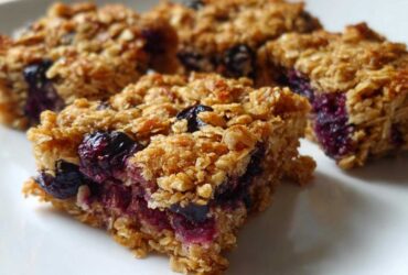 Close-up of several golden-brown Blueberry Baked Oatmeal Squares with visible baked blueberries on a white plate.