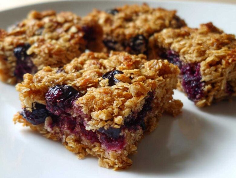 Close-up of several golden-brown Blueberry Baked Oatmeal Squares with visible baked blueberries on a white plate.