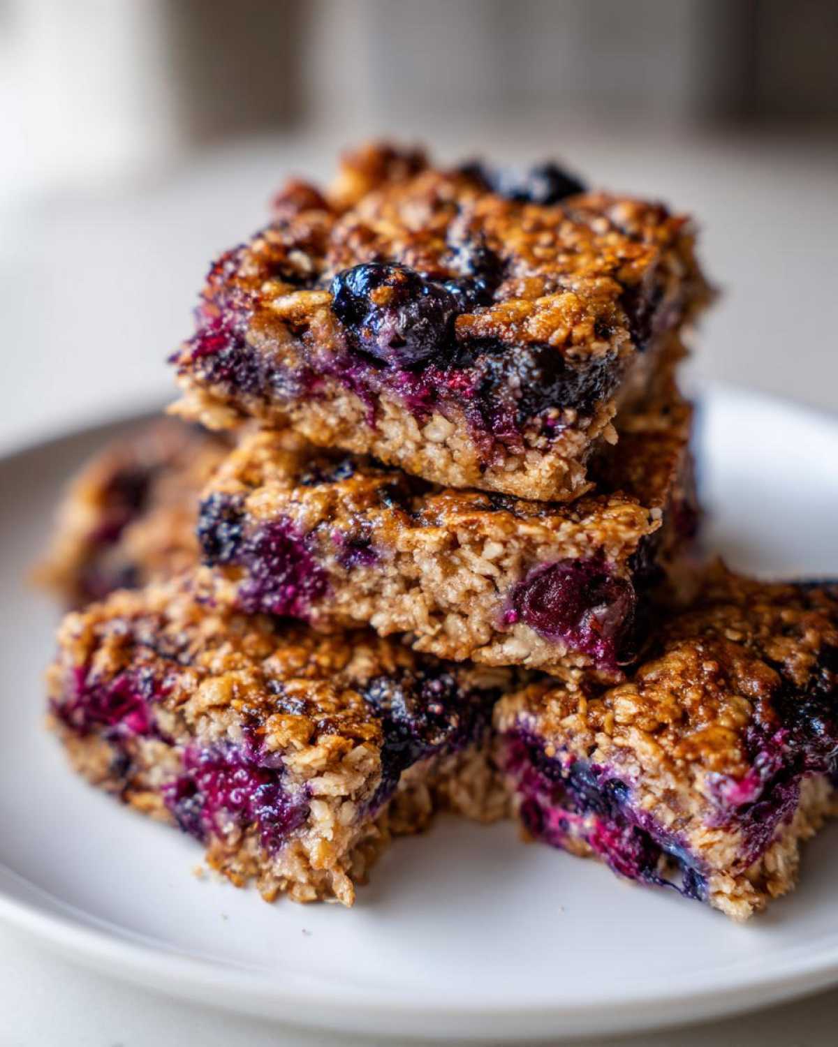 A stack of four moist Blueberry Baked Oatmeal Squares showing visible oats and bursting blueberries.