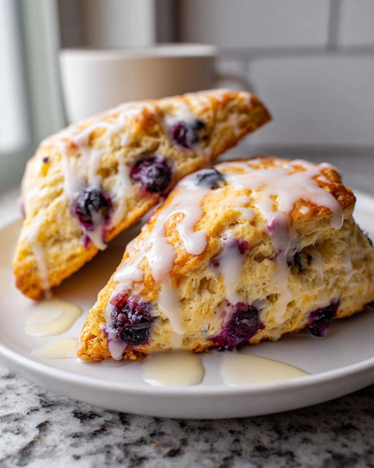 Two freshly baked Blueberry Lemon Scones topped with a thick white glaze, resting on a white plate.