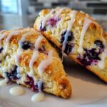 Two freshly baked Blueberry Lemon Scones drizzled with white icing, sitting on a white plate.