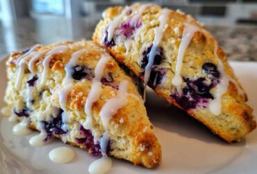 Two freshly baked Blueberry Lemon Scones drizzled with white icing, sitting on a white plate.