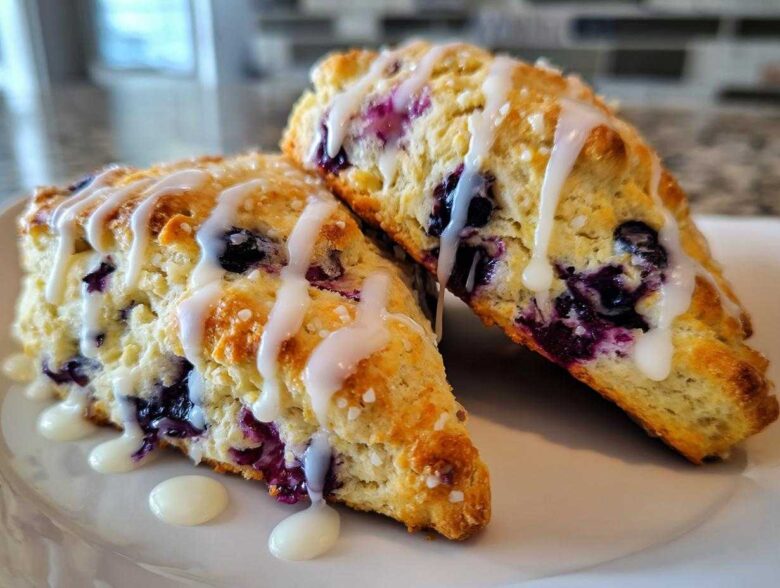 Two freshly baked Blueberry Lemon Scones drizzled with white icing, sitting on a white plate.