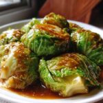 Steamed cabbage rolls covered in a rich garlic ginger sauce, served on a white plate.