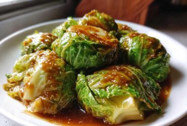Steamed cabbage rolls covered in a rich garlic ginger sauce, served on a white plate.