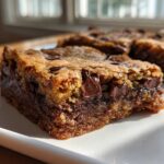 A close-up, tempting shot of a thick, chewy chocolate chip cookie bar showing melted chocolate chunks.