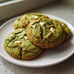 Four freshly baked Chewy Matcha White Chocolate Cookies with visible white chocolate chips, resting on a white plate.