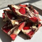 A stack of broken pieces of Chocolate Covered Strawberry Bark featuring dark and white chocolate swirls and fresh strawberries.