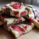 A close-up stack of broken pieces of Chocolate Covered Strawberry Bark featuring white chocolate, dark chocolate swirls, and bright red strawberry slices.
