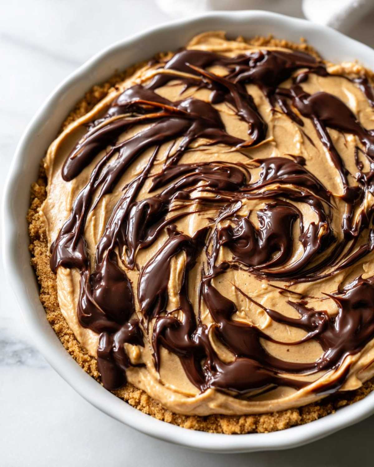 Close-up of a creamy Chocolate Peanut Butter Cheesecake Dip with a graham cracker crust and chocolate drizzle.