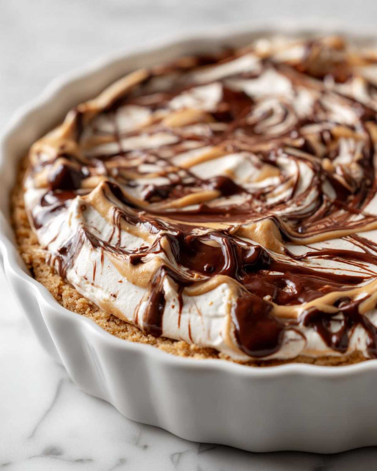 Close-up of Chocolate Peanut Butter Cheesecake Dip topped with swirled chocolate and peanut butter sauces in a white fluted dish.