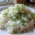 A mound of fluffy white Cilantro Lime Rice topped with fresh lime zest and chopped cilantro, served with a lime wedge.