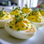 Close-up of perfectly piped Classic Deviled Eggs with Dill Pickle Relish, garnished with fresh thyme.