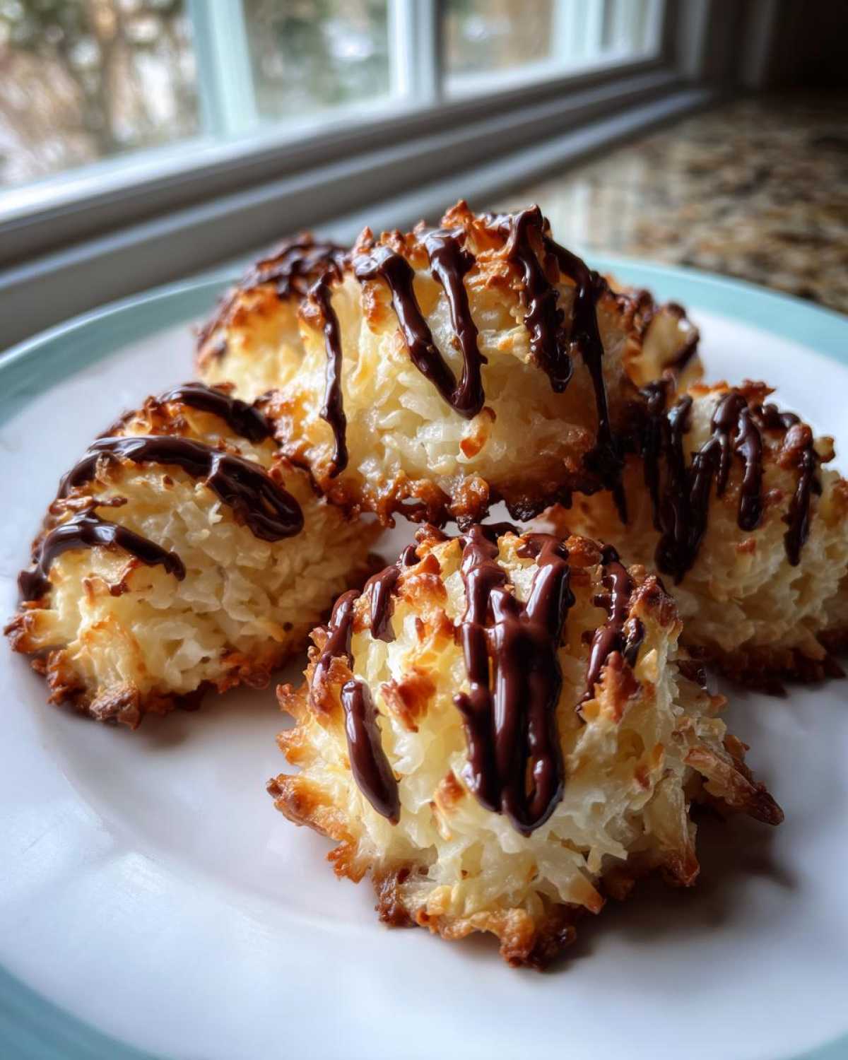A plate of golden brown Coconut Macaroons with Dark Chocolate Drizzle, set near a window.