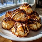 A stack of golden-brown Coconut Macaroons with Dark Chocolate Drizzle piled high on a white plate.