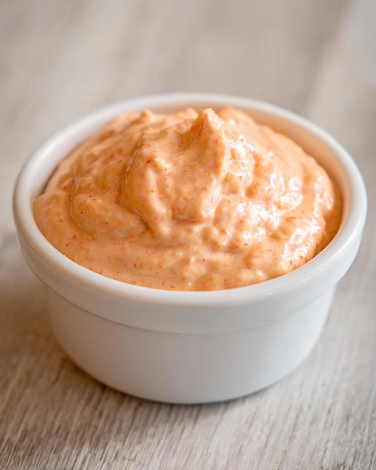 A close-up of thick, creamy, orange-hued Copycat Raising Cane’s Sauce served in a small white ramekin.