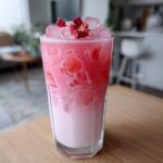 A tall glass filled with a layered Copycat Starbucks Pink Drink, featuring pink liquid, ice cubes, and dried fruit garnish.