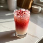 A tall glass of layered Copycat Starbucks Pink Drink, topped with ice and dried rose petals.