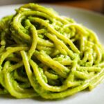 A close-up shot of thick pasta noodles coated in vibrant green Creamy Avocado Pasta sauce on a light plate.