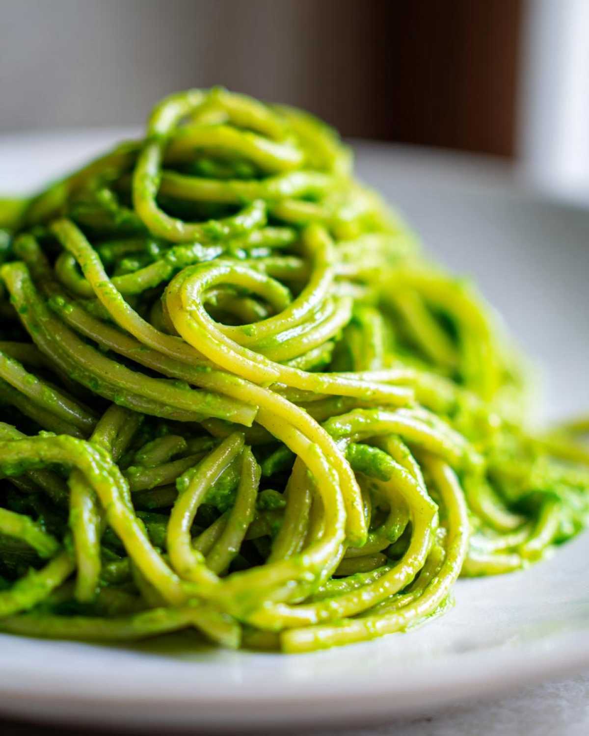 A close-up shot of spaghetti noodles coated thickly in vibrant green Creamy Avocado Pasta sauce, served on a white plate.