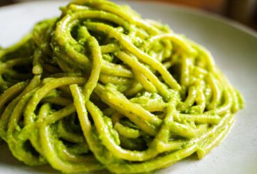A close-up shot of thick pasta noodles coated in vibrant green Creamy Avocado Pasta sauce on a light plate.