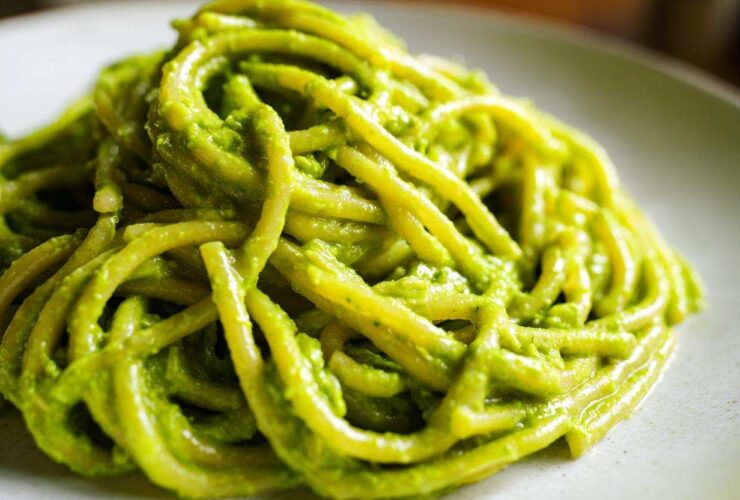 A close-up shot of thick pasta noodles coated in vibrant green Creamy Avocado Pasta sauce on a light plate.