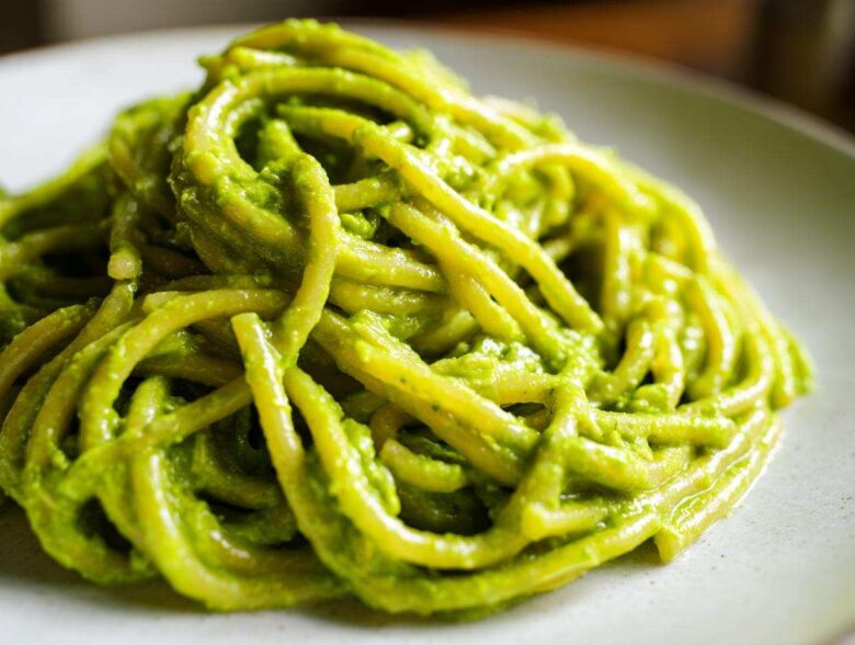 A close-up shot of thick pasta noodles coated in vibrant green Creamy Avocado Pasta sauce on a light plate.