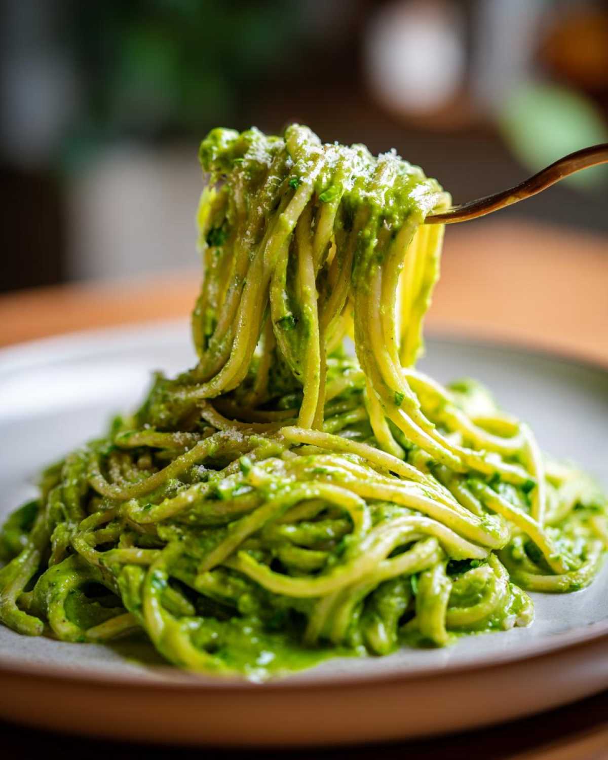 A fork lifting a generous portion of bright green Creamy Avocado Pasta from a plate, showing rich sauce coating the noodles.