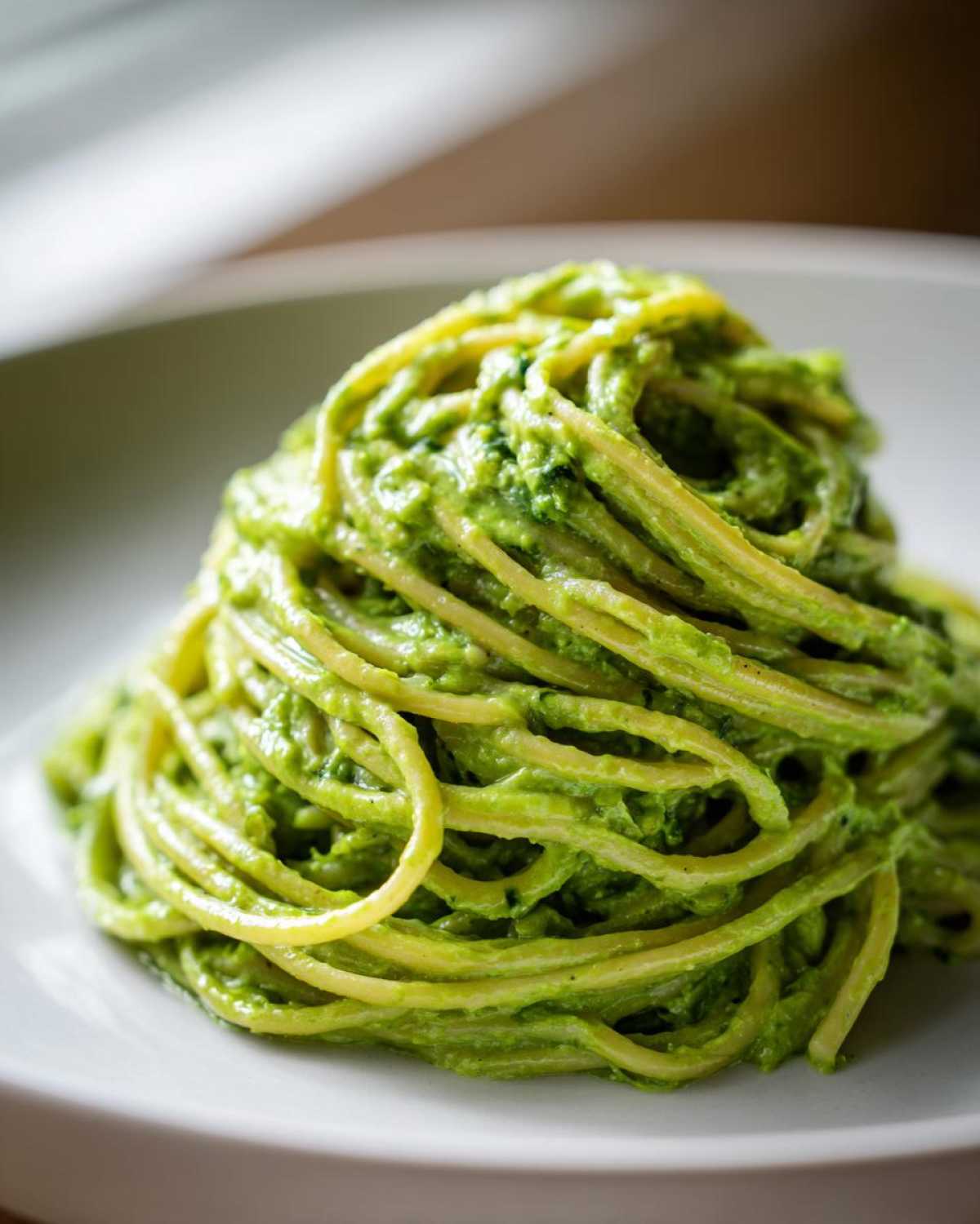 A mound of spaghetti tossed in vibrant green Creamy Avocado Pasta sauce served on a white plate.