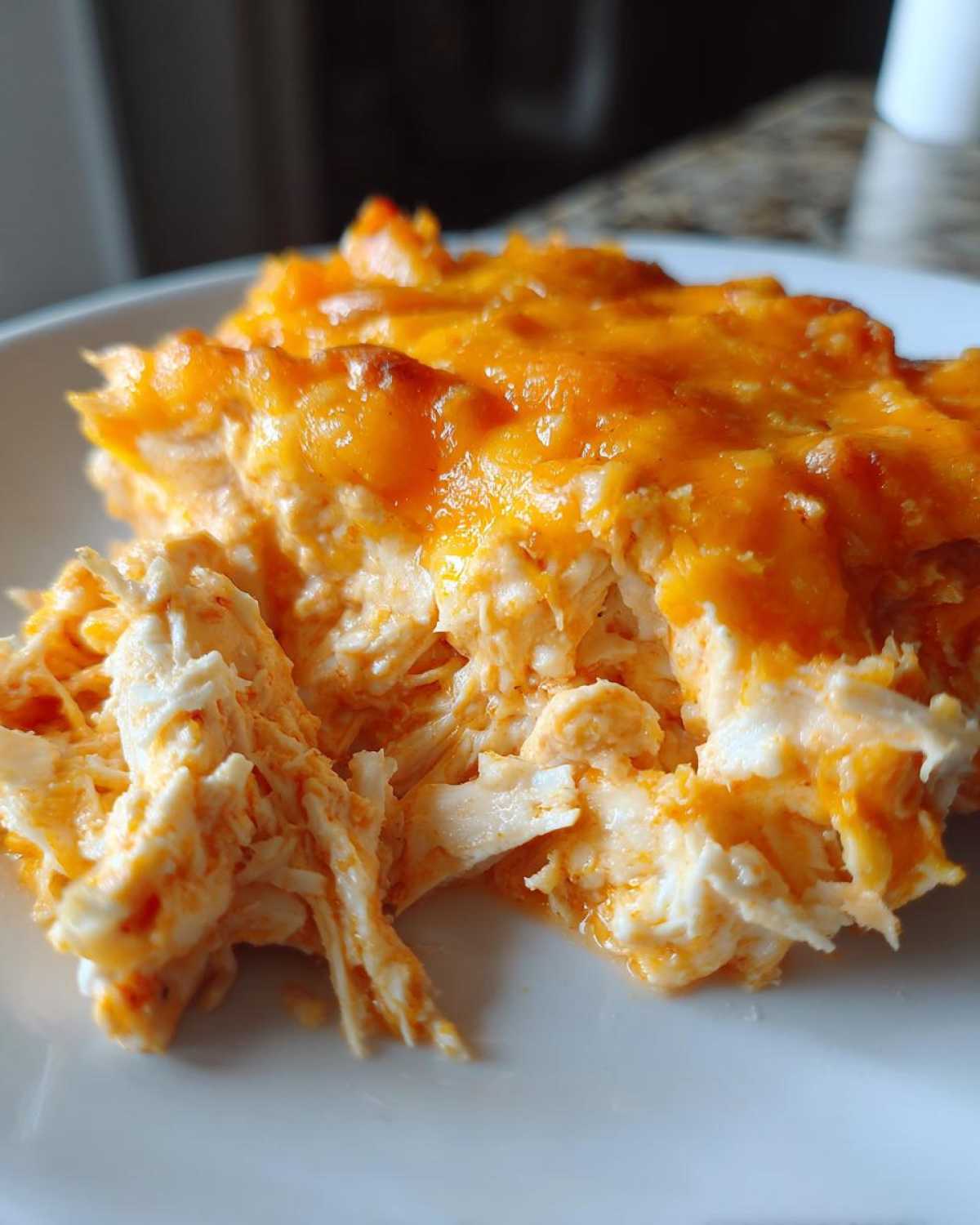 A close-up serving of creamy, shredded chicken mixed with orange sauce and topped with melted cheddar cheese, representing Baked Buffalo Chicken Dip.