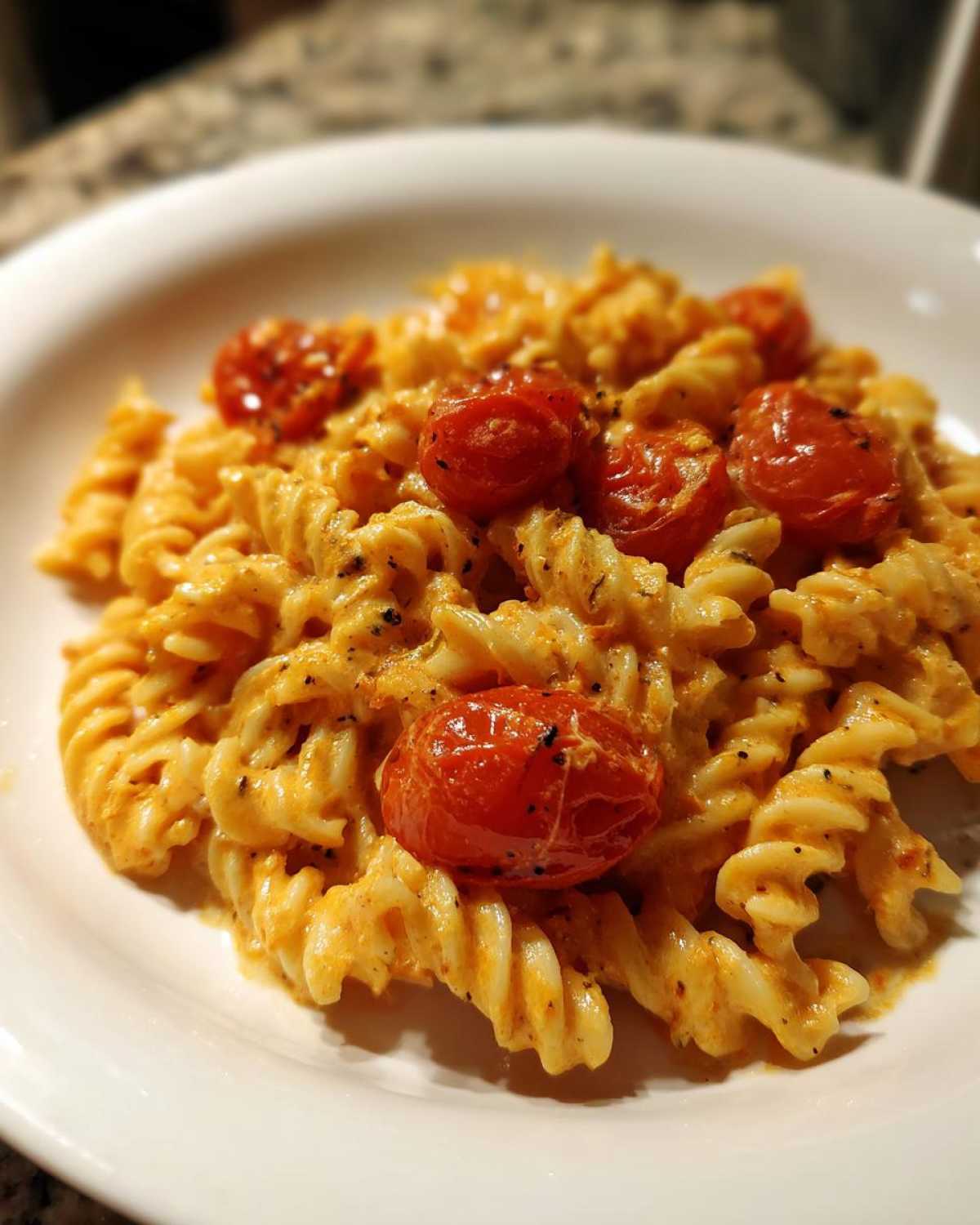 Close-up of a serving of Baked Feta Pasta with fusilli noodles coated in a creamy orange sauce and topped with roasted cherry tomatoes.