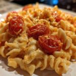 Close-up of creamy Baked Feta Pasta with fusilli noodles coated in orange sauce and topped with roasted cherry tomatoes.