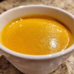 Close-up of a white bowl filled with vibrant orange Creamy Coconut Lentil Soup.
