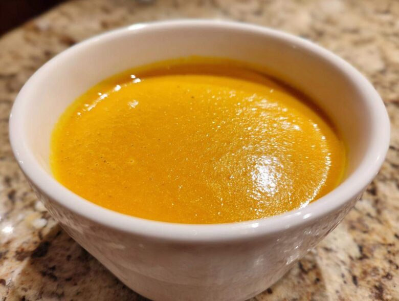 Close-up of a white bowl filled with vibrant orange Creamy Coconut Lentil Soup.