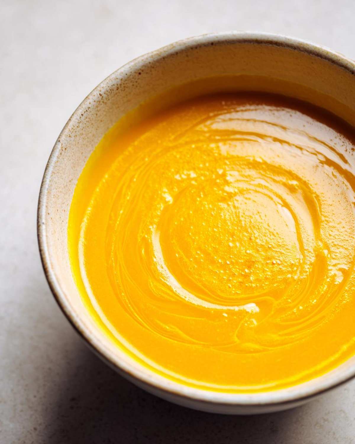 Overhead close-up of a vibrant orange Creamy Coconut Lentil Soup swirled in a rustic ceramic bowl.