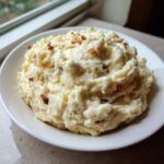 A close-up of a white bowl filled with fluffy Creamy Garlic Mashed Cauliflower, topped with crispy brown bits.