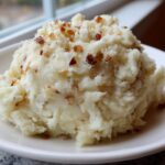 A generous scoop of Creamy Garlic Mashed Cauliflower topped with crispy bits, served on a white plate.