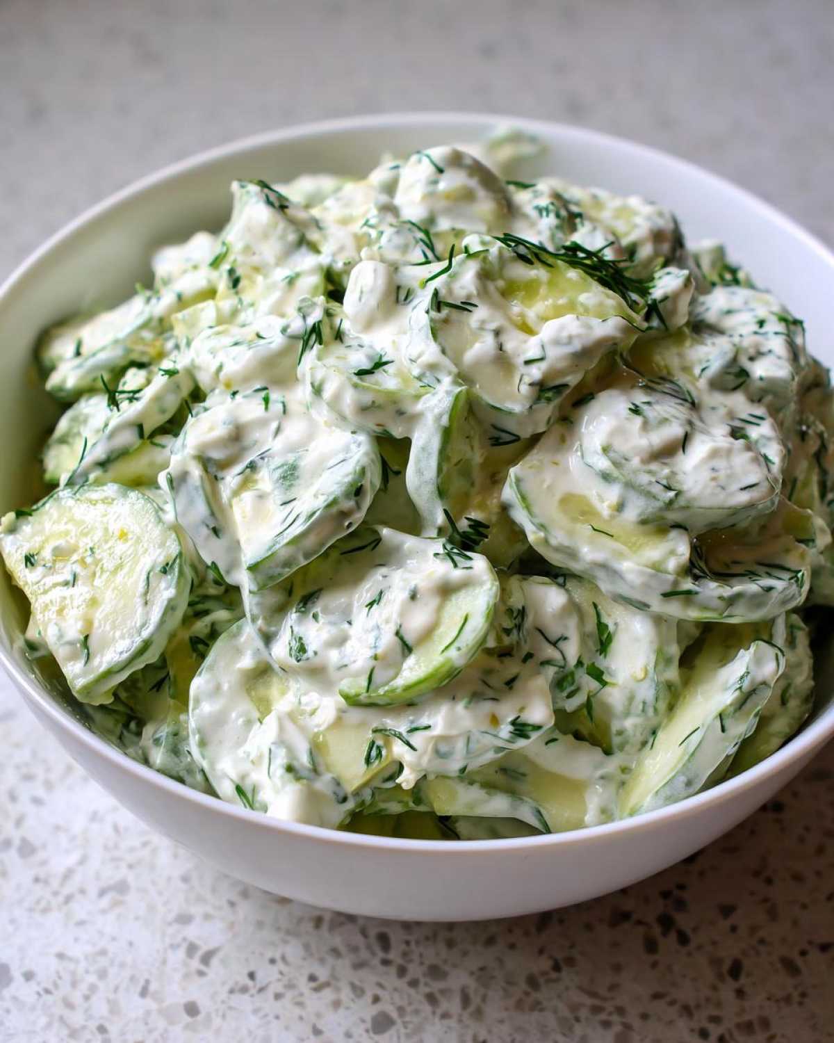 Close-up of sliced cucumbers coated in a rich, creamy dressing and fresh dill, ready to serve as Creamy German Cucumber Salad.