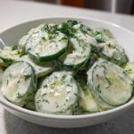 Close-up of sliced cucumbers coated in a creamy dressing and fresh dill, representing Creamy German Cucumber Salad.