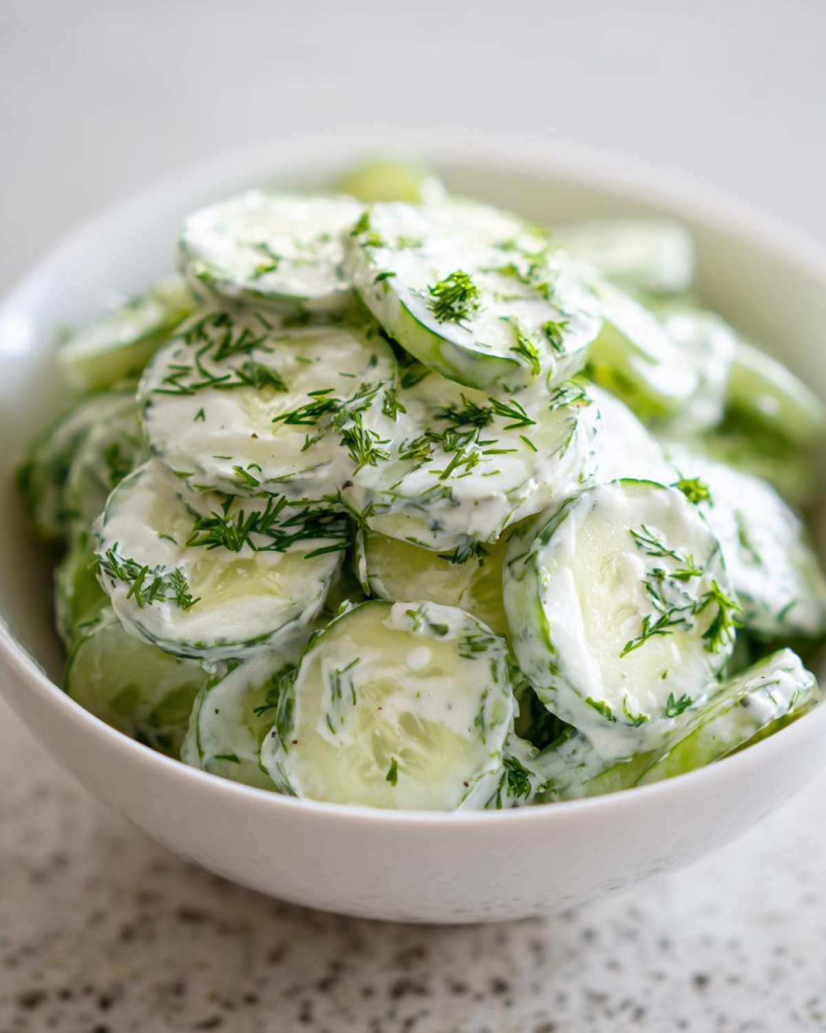 Close-up of thinly sliced cucumbers coated in a creamy dressing and topped with fresh dill, ready to serve as Creamy German Cucumber Salad.