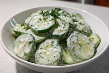 Close-up of sliced cucumbers coated in a creamy dressing and fresh dill, representing Creamy German Cucumber Salad.