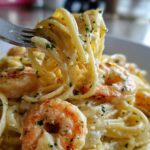 A fork twirls linguine coated in rich sauce, featuring plump shrimp in Creamy Lemon Garlic Shrimp Pasta.