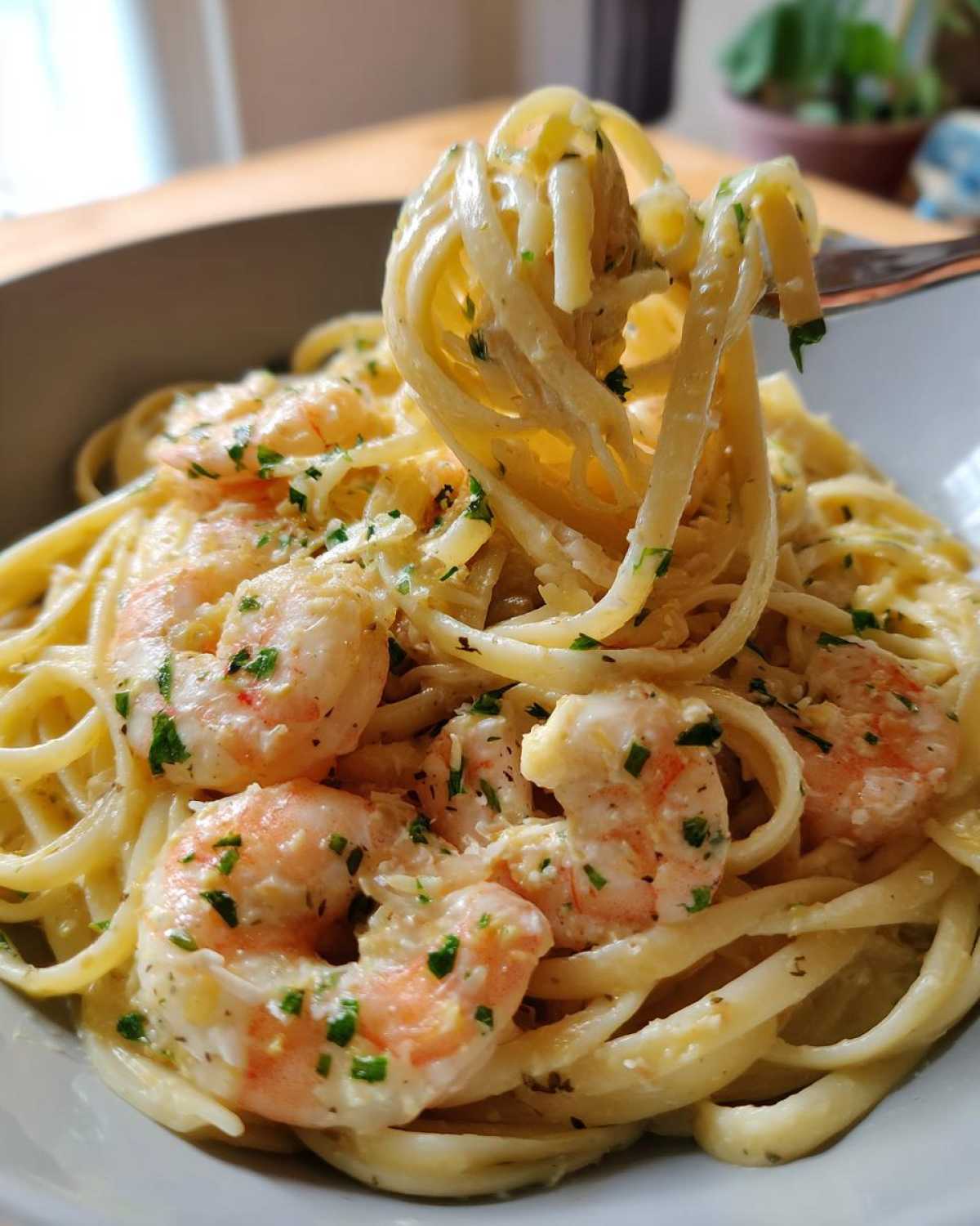 A fork lifting linguine noodles coated in sauce with plump shrimp from a bowl of Creamy Lemon Garlic Shrimp Pasta.