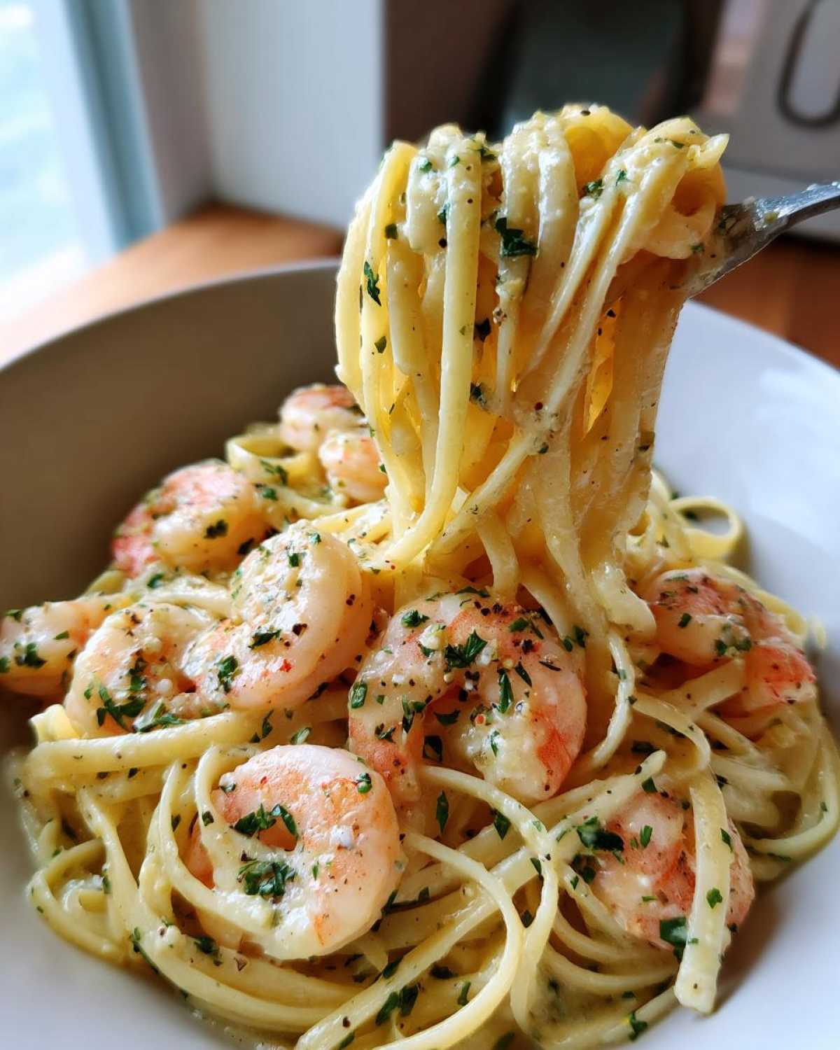 A fork lifts a generous portion of fettuccine coated in creamy sauce, mixed with plump shrimp, in a bowl of Creamy Lemon Garlic Shrimp Pasta.