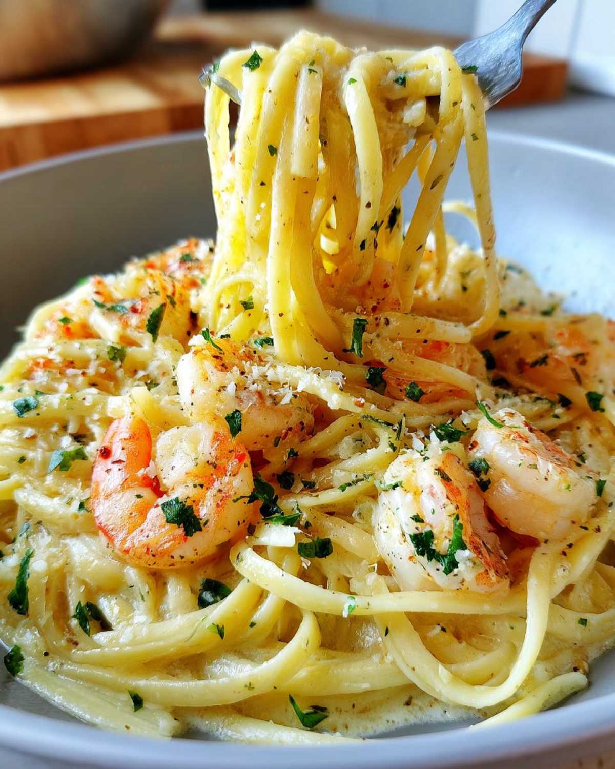 A fork twirls linguine pasta coated in creamy sauce, shrimp, and parsley from a bowl of Creamy Lemon Garlic Shrimp Pasta.