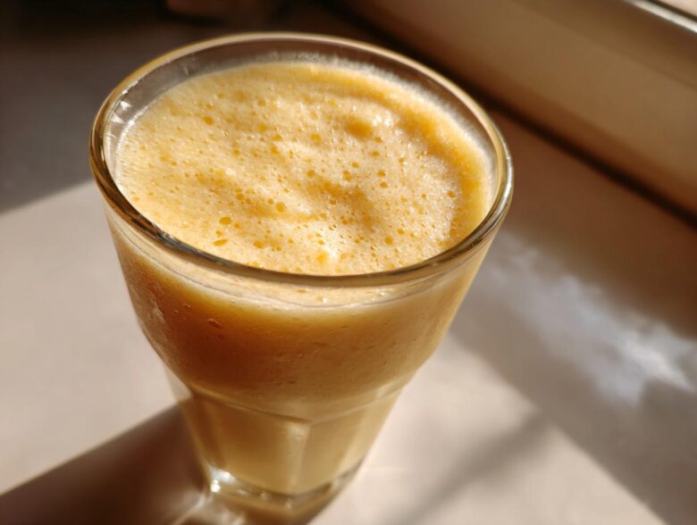 Close-up of a frothy, creamy Pineapple Coconut Smoothie in a tall glass, catching bright sunlight.