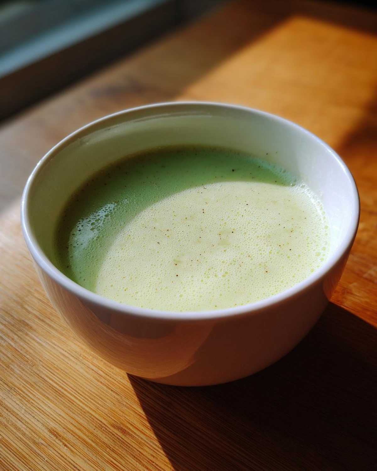 Close-up of a white bowl filled with light green Creamy Potato Leek Soup, showing a frothy top.