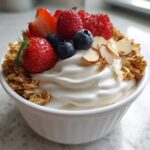 Close-up of a thick Creamy Vanilla Protein Smoothie Bowl topped with fresh strawberries, raspberries, blueberries, granola, and sliced almonds.