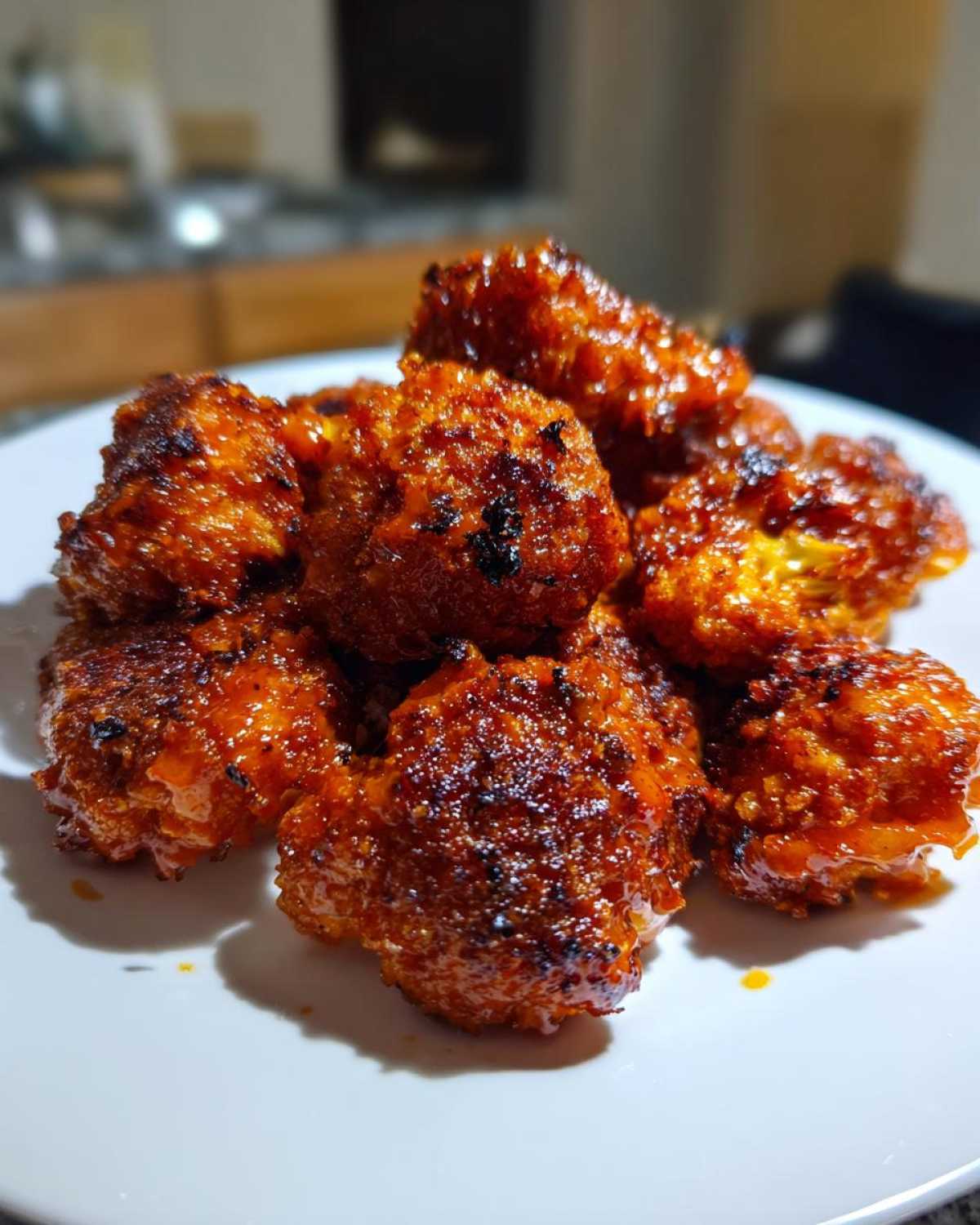 A close-up shot of several dark orange, glossy Crispy Air Fryer Cauliflower Wings piled on a white plate.
