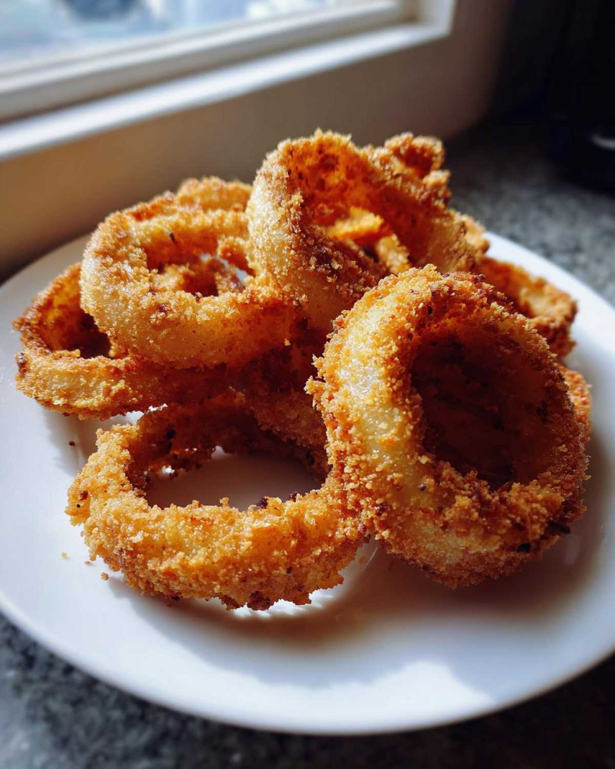 A close-up of several golden brown and crispy Air Fryer Onion Rings piled on a white plate.